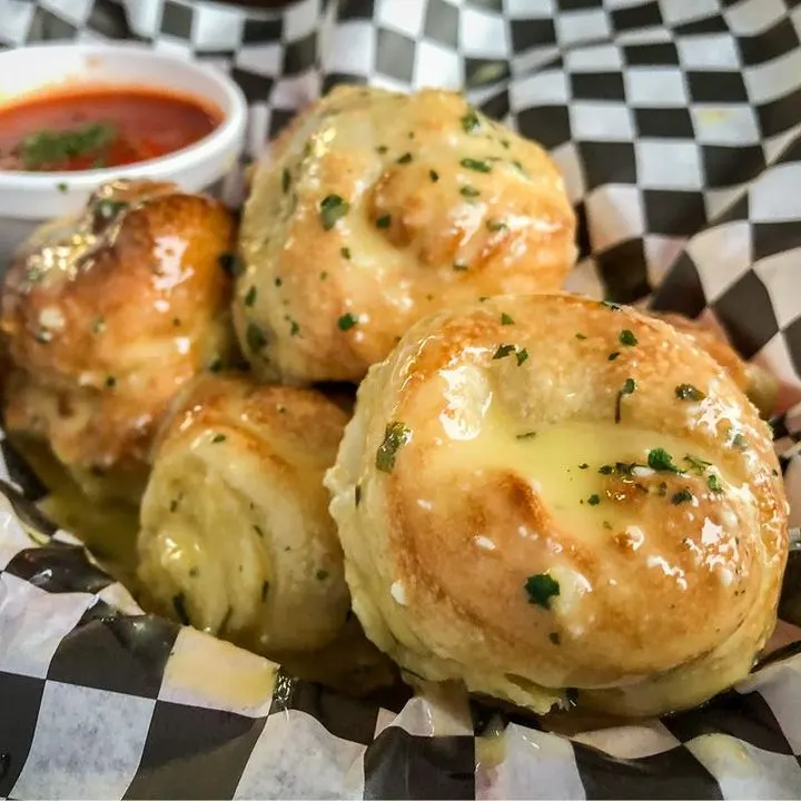 A basket of golden garlic knots with marinara for dipping