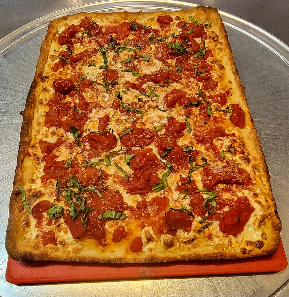 A grandma-style pie with crushed tomato and fresh basil